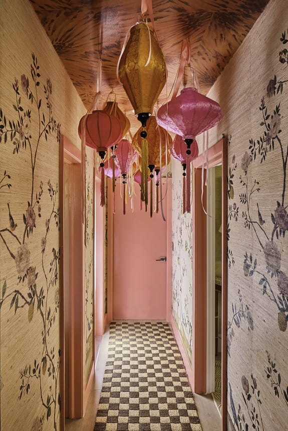 Colorful paper lanterns hang in a floral wallpapered hallway with pink doors and a checkered floor.