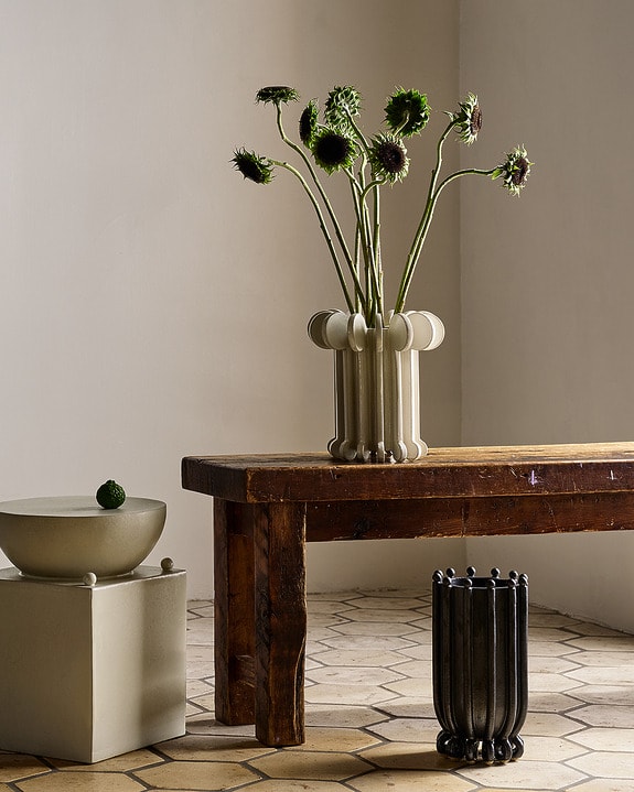 Wooden table with a ceramic vase of thistles, next to bowls and a decorative piece on tiled floor.