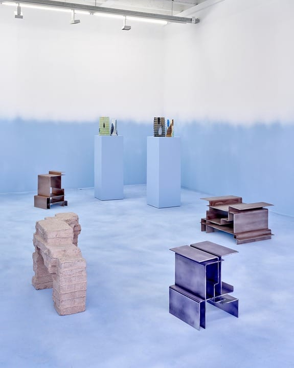 Art gallery with modern sculptures on pedestals and floor, featuring geometric shapes and a blue-themed interior design.