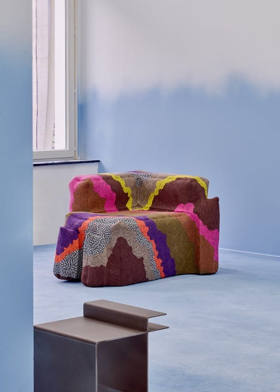 Colorful abstract-patterned armchair in a minimalist room with blue walls and a window.