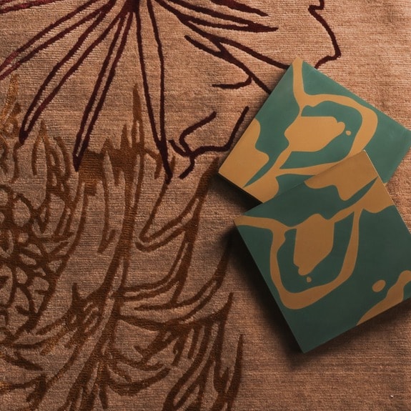 Two green and orange square tiles resting on a textured brown patterned fabric with abstract floral designs.