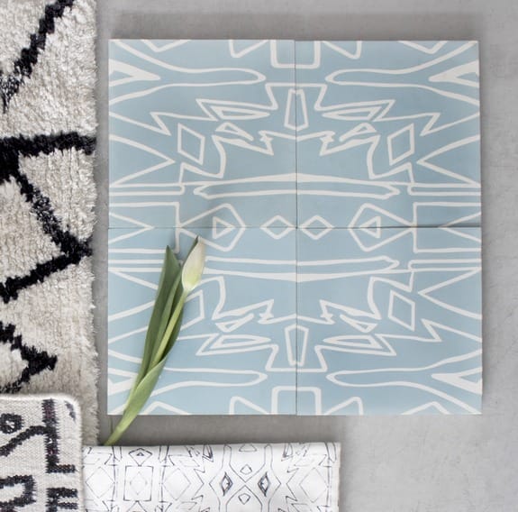 Blue and white geometric patterned tiles on a gray surface with a single white tulip and black patterned rugs nearby.