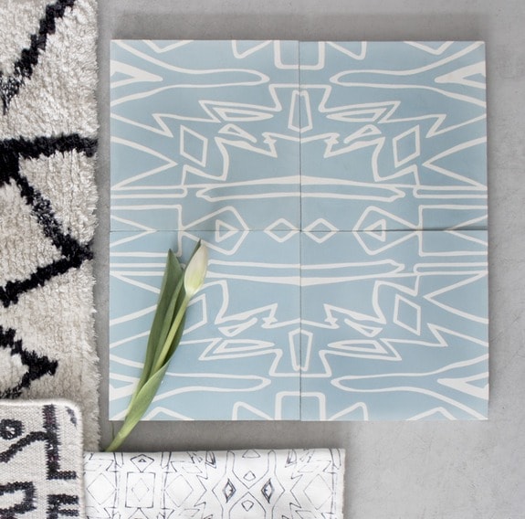 Blue and white geometric patterned tiles on a gray surface with a single white tulip and black patterned rugs nearby.