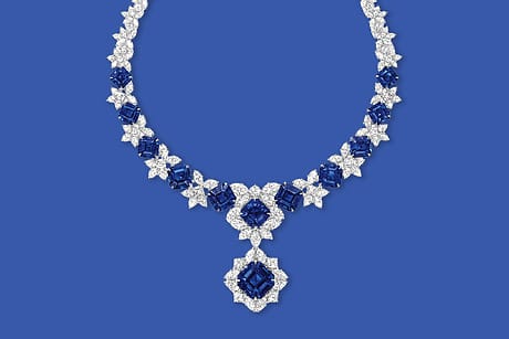 Diamond and sapphire necklace with intricate floral design displayed on a blue background.