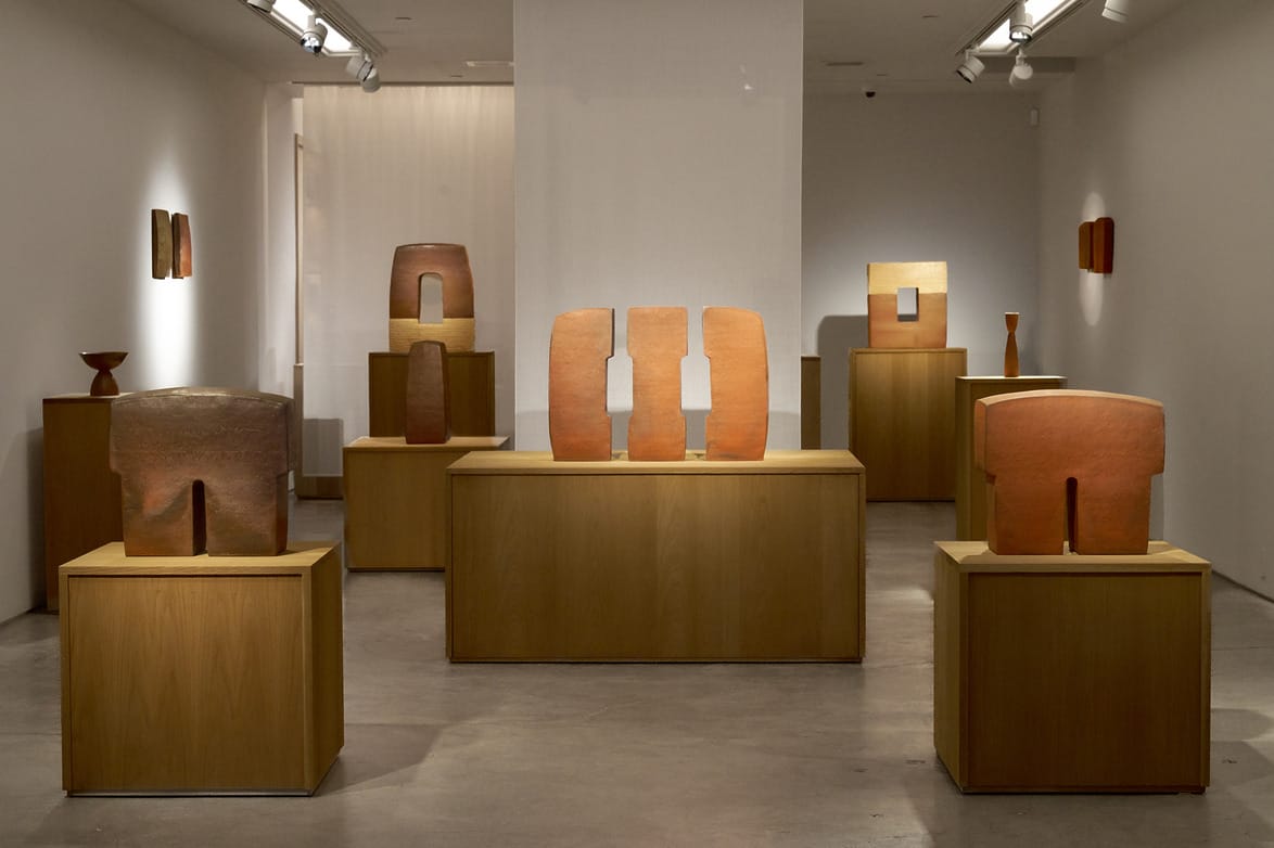 Art gallery displaying various modern sculptures on wooden pedestals against a minimalist interior with soft lighting.