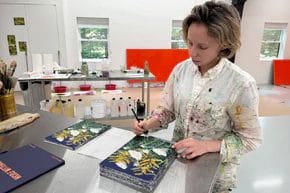 Artist painting botanical prints in a studio filled with art supplies and canvas.