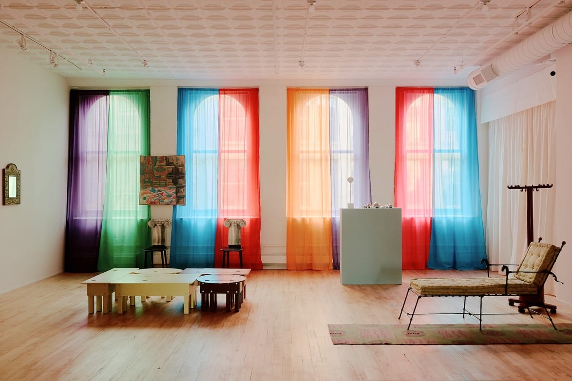 Colorful room with rainbow curtains, abstract art, wooden tables, and a cushioned bench on a light wooden floor.