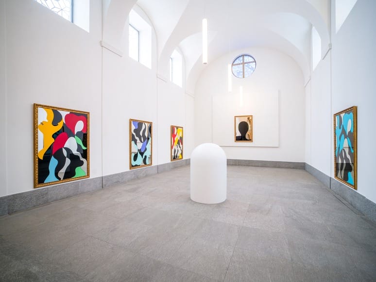 Contemporary art gallery with colorful abstract paintings on white walls and a central white sculptural piece.