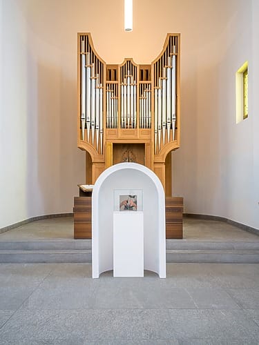 Modern church interior with a large wooden pipe organ and a minimalist art display on a white pedestal in the foreground