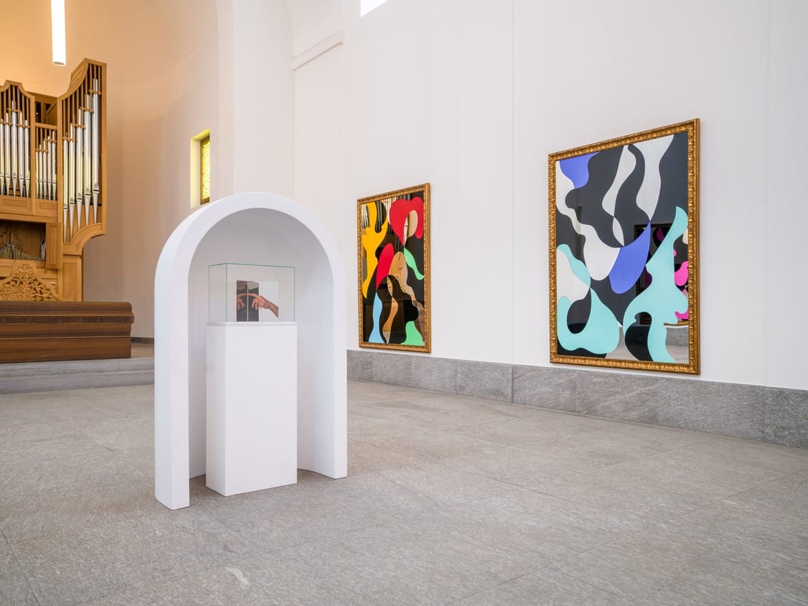 Art gallery interior with abstract paintings on the wall and a small sculpture in a white archway display.