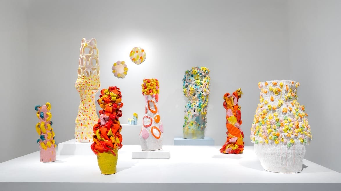 Colorful ceramic sculptures with vibrant textures displayed on white pedestals in a bright gallery space.