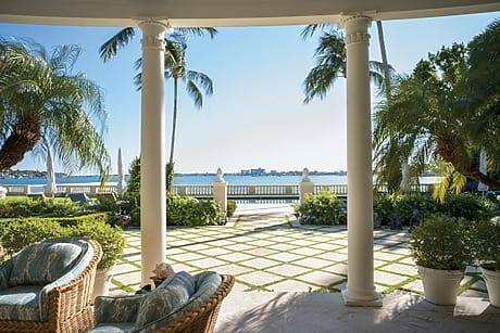 Tropical patio with wicker furniture, overlooking a serene ocean view, framed by palm trees on a sunny day.