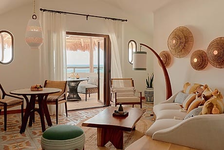 Cozy living room with wooden furniture, wall decor, and a view of an outdoor patio with ocean in the background.