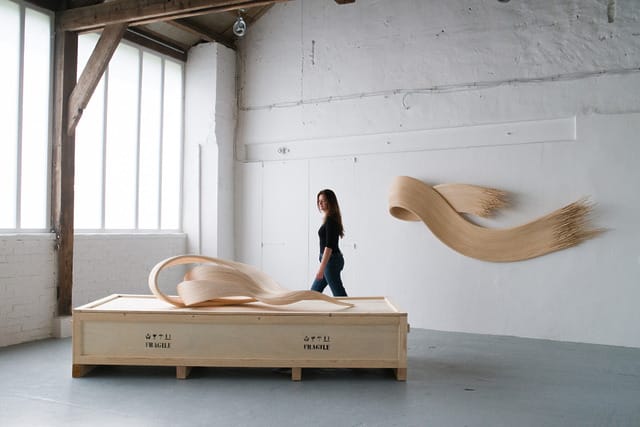 Woman walking past abstract wooden sculptures in an industrial-style white gallery space
