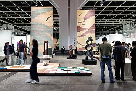People walking through a modern art exhibition with sculptures and large patterned panels under industrial lighting.