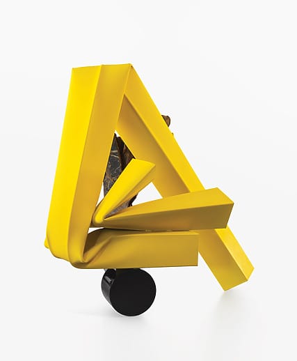 Abstract sculpture with intertwined yellow and gold geometric shapes on a black cylindrical base against a white background