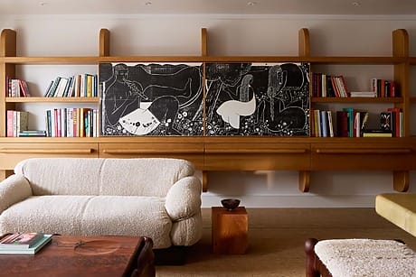 Chic living room with wooden bookshelf, abstract artwork, cozy beige sofa, and a variety of colorful books on display.