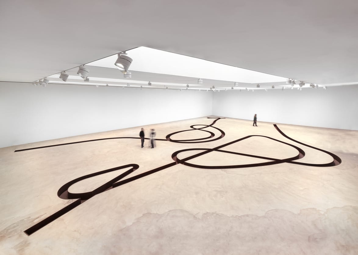 Spacious art gallery with abstract black line installation on the floor, visitors observing the artwork.