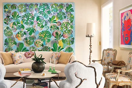Living room with colorful leaf-patterned wall art, plush seating, vintage chairs, floral accents, and vibrant framed portrait.