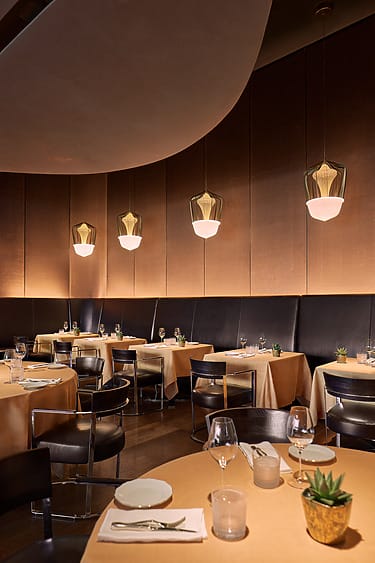 Elegant restaurant interior at Bulgari hotel in Milan with dim lighting, modern pendant lights, and tables set with white dishes and glassware.