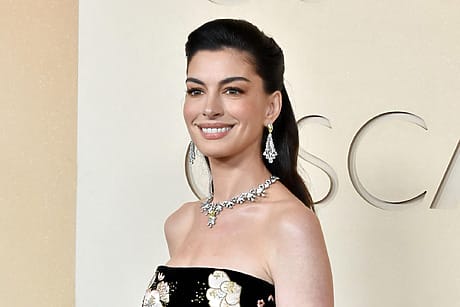 Person smiling, wearing a black floral dress and jewelry, at a formal event.