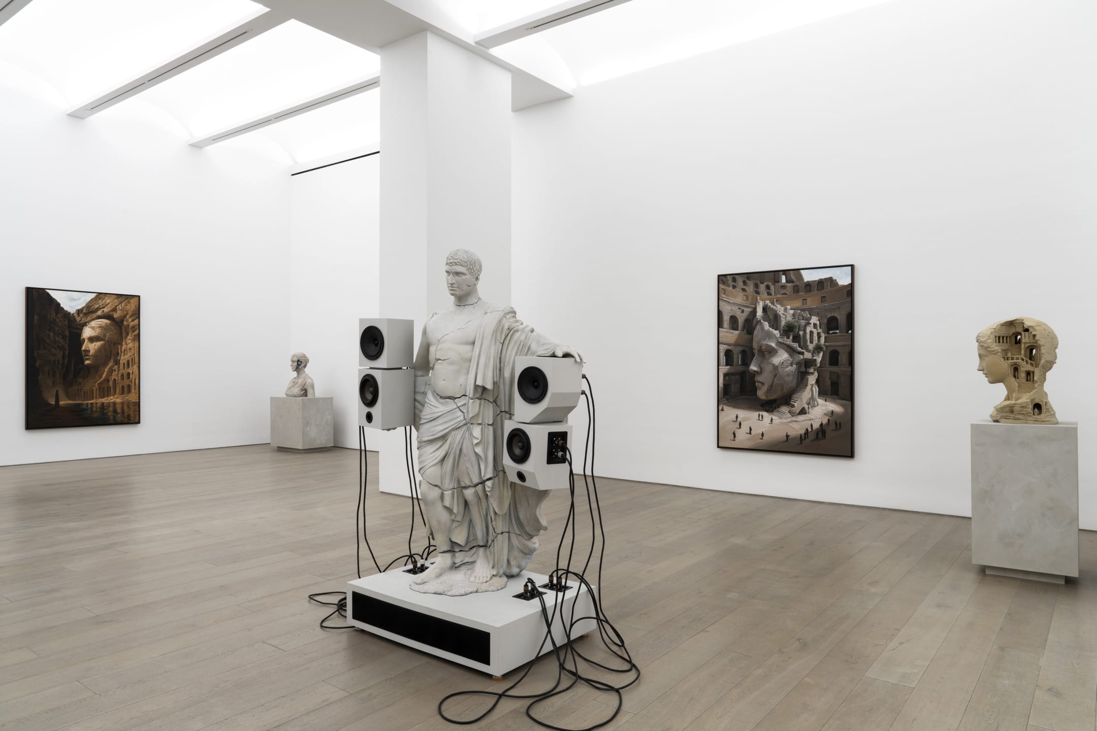 Modern art exhibit with classical statue wired to speakers, surrounded by three large framed photographs on gallery walls.