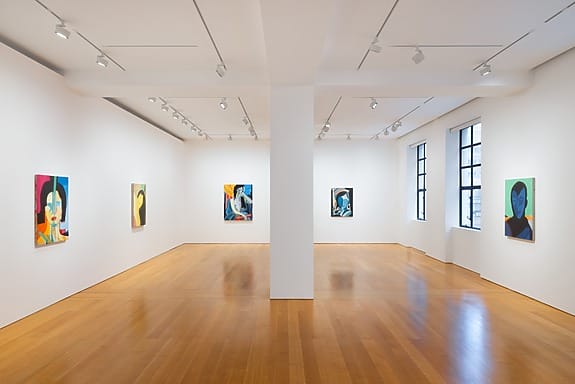 Art gallery interior with colorful abstract paintings on white walls and wooden flooring.