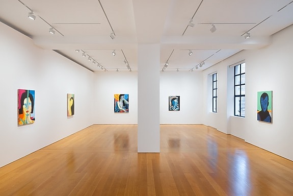 Art gallery interior with colorful abstract paintings on white walls and wooden flooring.