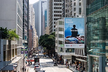 Busy Hong Kong street with tall buildings and a large billboard displaying "Art is vision" with a person silhouette.