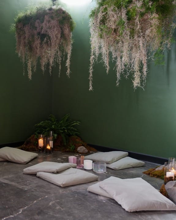 Meditation room with green walls, hanging plants, candles, and cushions on the floor for seating and relaxation.