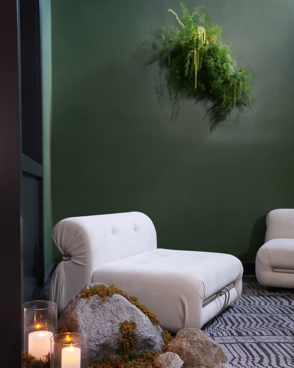 Modern lounge with white chairs, green wall, a fern, and rocks with lit candles creating a cozy ambiance