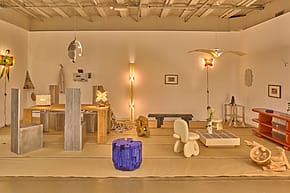 Contemporary art installation featuring abstract sculptures and modern furnishings in a minimalist gallery space.