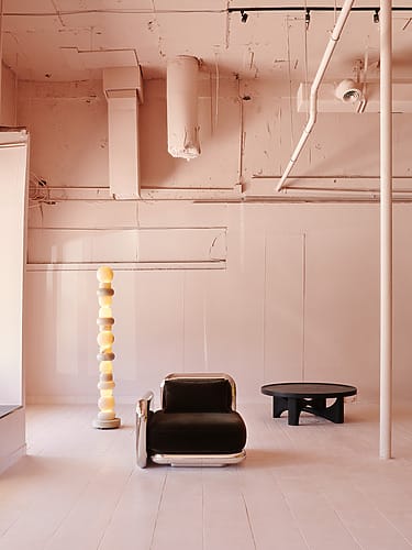 Minimalist interior with a black chair, unique floor lamp, and a small table on a light wooden floor.