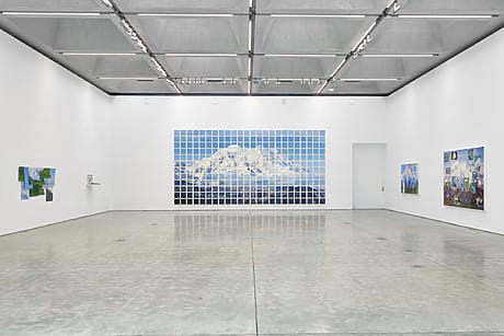 Art gallery with modern paintings on white walls, featuring a large tiled mountain artwork and smaller abstract pieces.