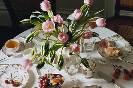 Table set for breakfast with pink tulips, tea, grapes, cherries, and bread on patterned china plates.