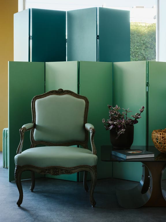 Elegant green armchair near modern metal screens and a stylish table with a plant in a contemporary setting.