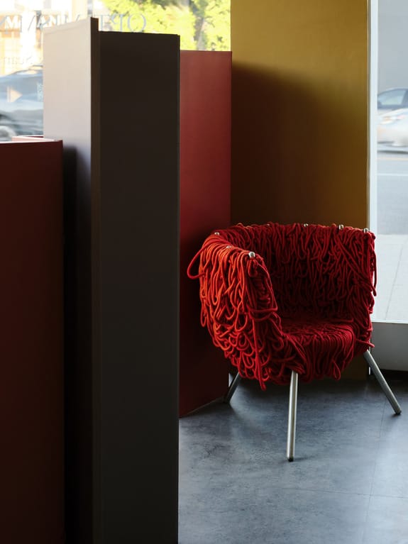 Modern red rope chair with metal legs in a corner of a contemporary room with large windows and neutral walls.
