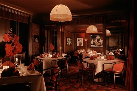 Dimly lit restaurant interior with white tablecloths, red napkins, and vintage decor, creating a warm and inviting atmosphere.