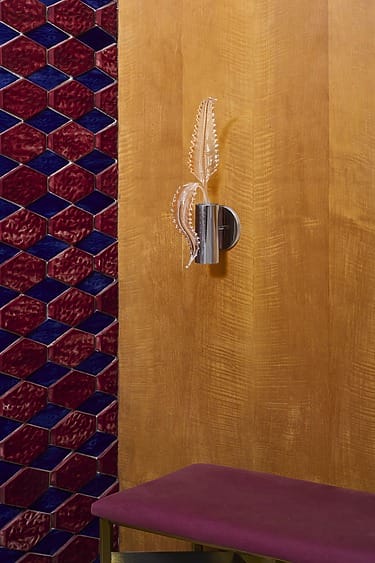 Red and blue geometric wall tiles with a patterned wooden wall and modern wall light above a magenta bench.