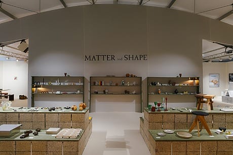 Art exhibition display featuring various ceramics and glassware on tiered shelves with "Matter and Shape" on the wall.