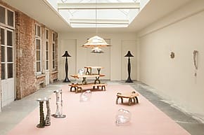Contemporary art installation with unique furniture and glass sculptures in a well-lit room with skylights and brick walls
