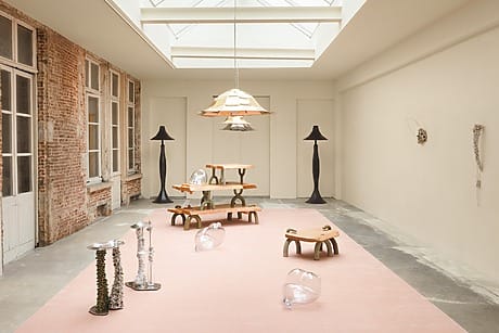 Contemporary art installation with unique furniture and glass sculptures in a well-lit room with skylights and brick walls