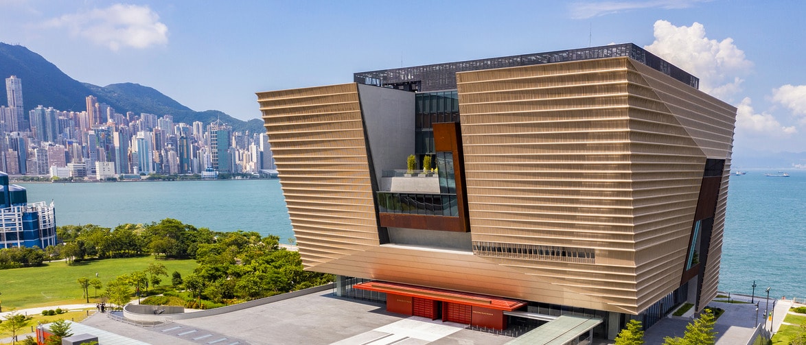 A modern Hong Kong waterfront building with a unique architectural design, set against a city skyline and mountains in the background.