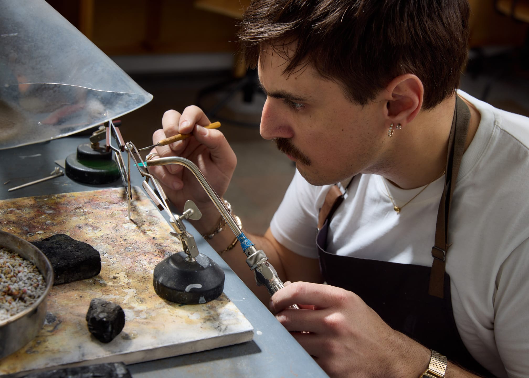 Artisan and designer Heath Wagoner focused on intricate metalworking, using tools and flame to shape tableware on a workbench.