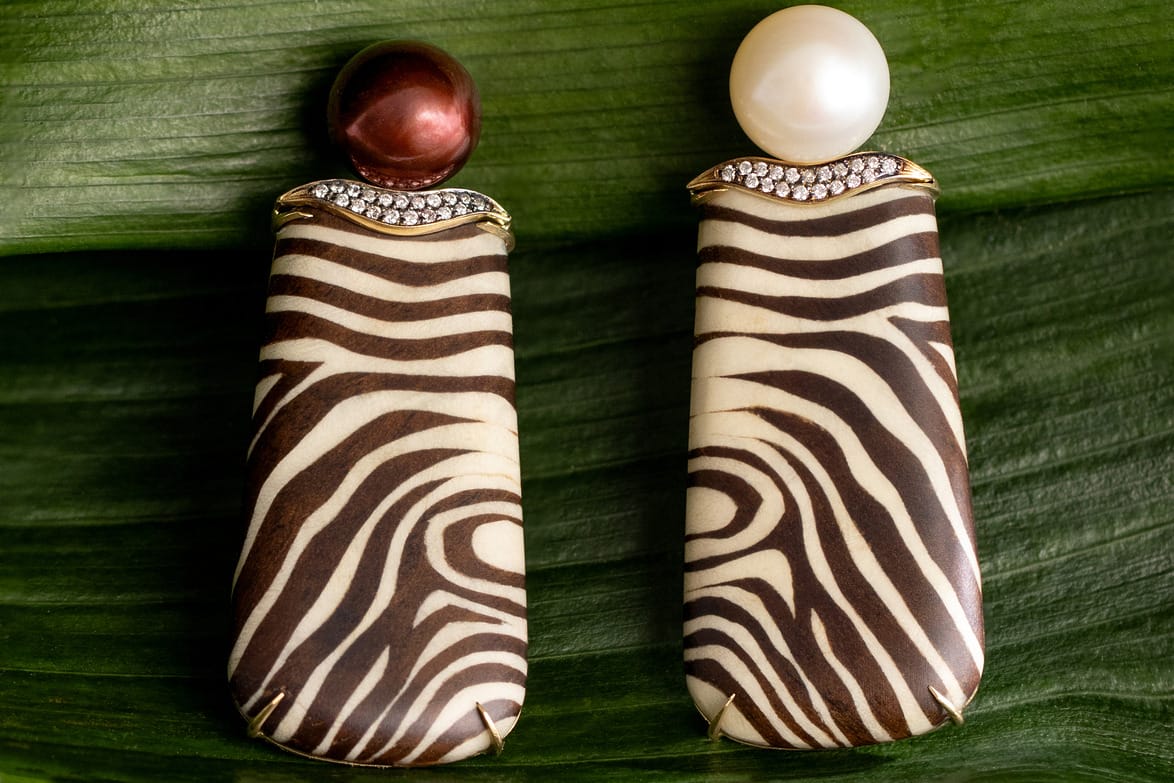 Elegant earrings with zebra print design, accented by a pearl and a red bead, displayed on a green leaf background.