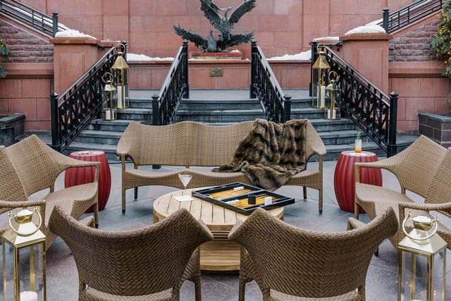 Outdoor seating area with wicker chairs, a fur throw, and a backgammon board, set against a stone staircase background.