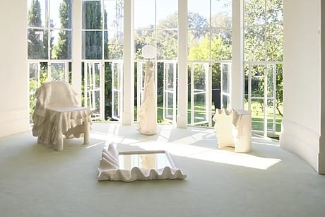 Minimalist room with sculptural furniture and large windows overlooking a garden, highlighting natural light and modern design.