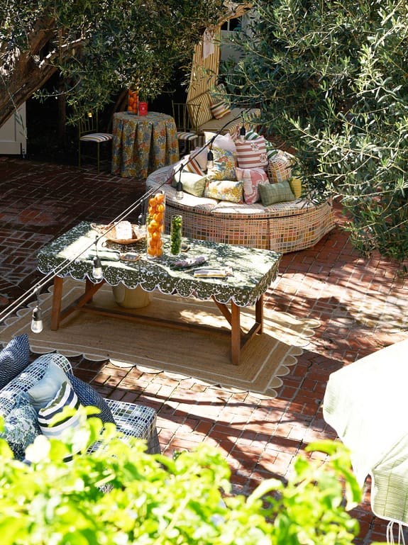 Outdoor patio with a table set for dining, surrounded by lush greenery, comfortable seating, and decorative cushions.