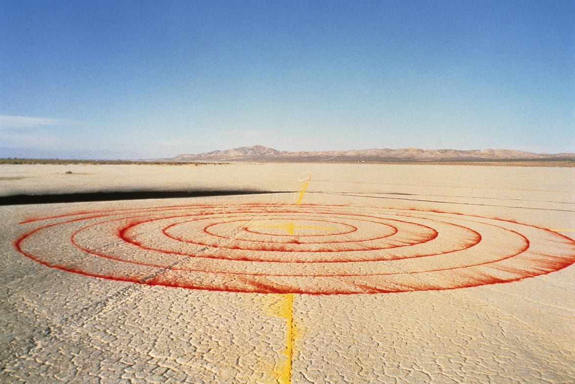 Red target circles painted on cracked desert ground under clear blue sky with distant mountains.