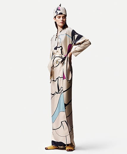 Person wearing a long, patterned beige outfit with abstract designs, standing against a plain background.